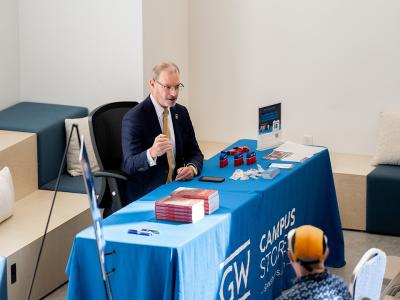 Todd Belt sitting at a GW campus store table, signing copies of his new book