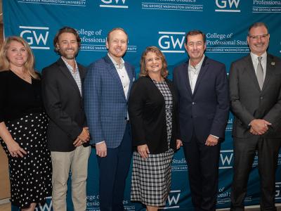 Lesley Lopez, Casey Burgat, Anthony Shop, Dean Riddle, Terry Szuplat, and Todd Belt smiling and posing in front of GW step-and-repeat