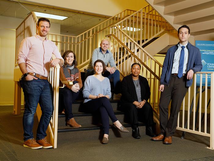Photo with 6 people, mix of men and women, posing by staircase with metal railings