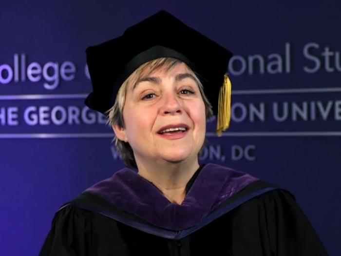 Toni Marsh wearing commencement gown and hat with tassel and part of College of Professional studies logo on a blue wall behind