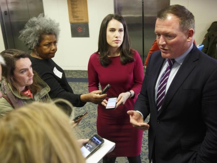 5 people standing near an elevator listening to a man in a blue suit and striped tie talking to them