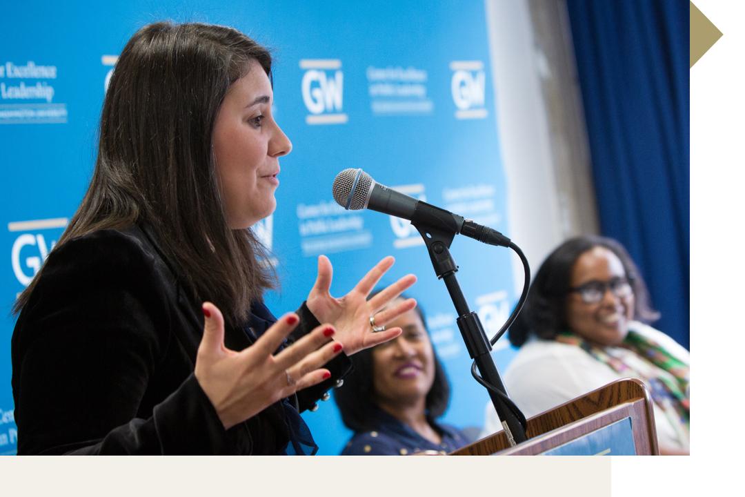 Woman speaking at podium with multiple GW logos behind her on backdrop
