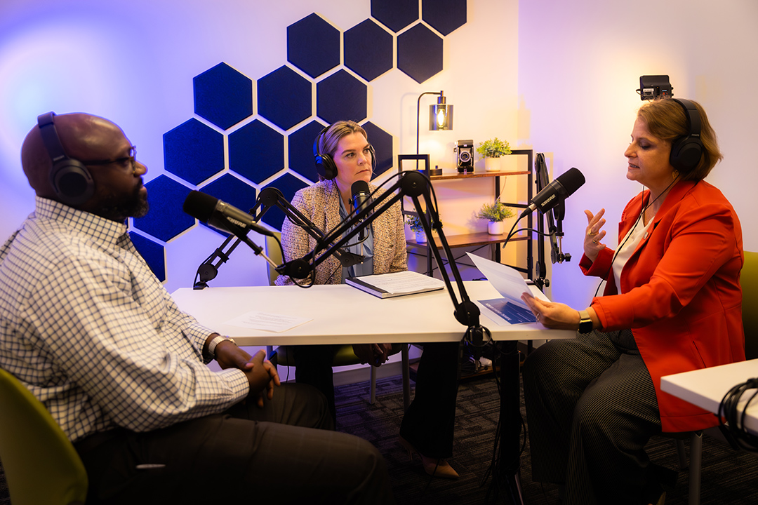 Three seated people recording podcast with large mic equipment on arms