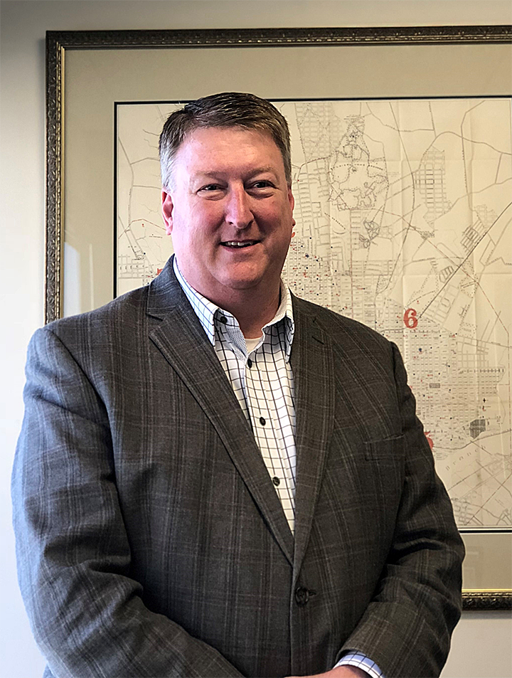 Keith Williams professional shot in gray suit with framed map behind him