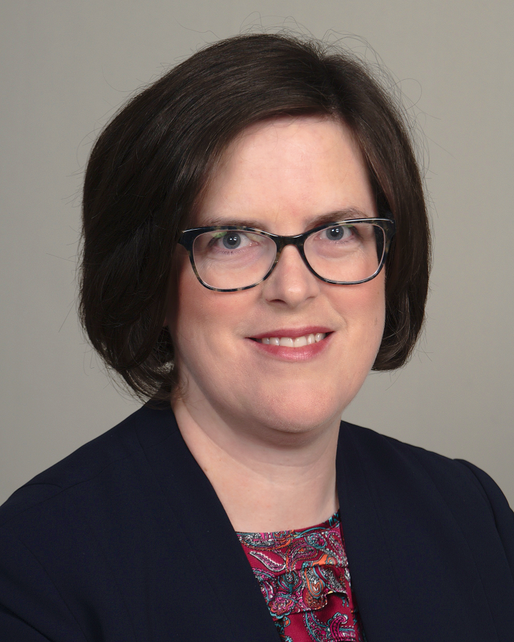 Woman with bobbed dark hair, glasses, black soft jacket and red paisley blouse