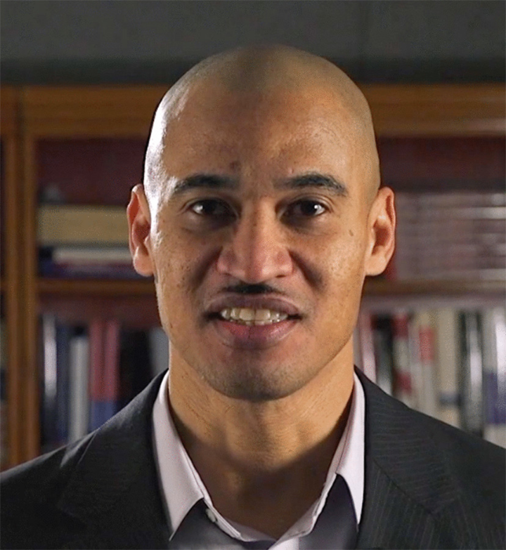 Slender clean shaven man with light brown skin in white collared shirt and gray pinstriped jacket