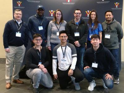 Group of 8 diverse students and 1 faculty member at the competition in a formal group photo.