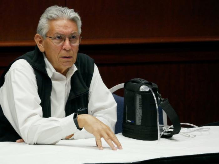 Kevin Gover speaks at GW, sitting at a table, white shirt, black vest, glasses