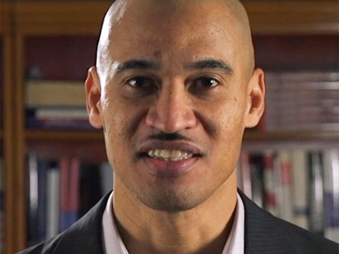 Slender clean shaven man with light brown skin in white collared shirt and gray pinstriped jacket