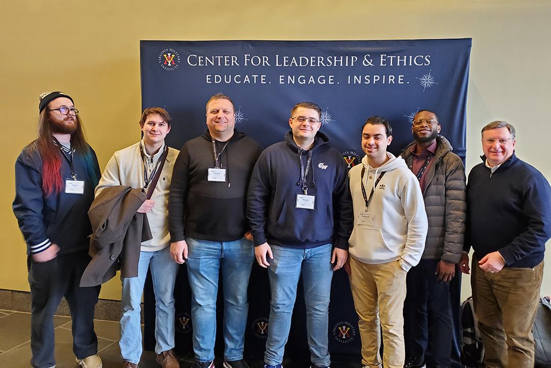 Student team of 6 plus professor posing in front of Center for Leadership & Ethics backdrop