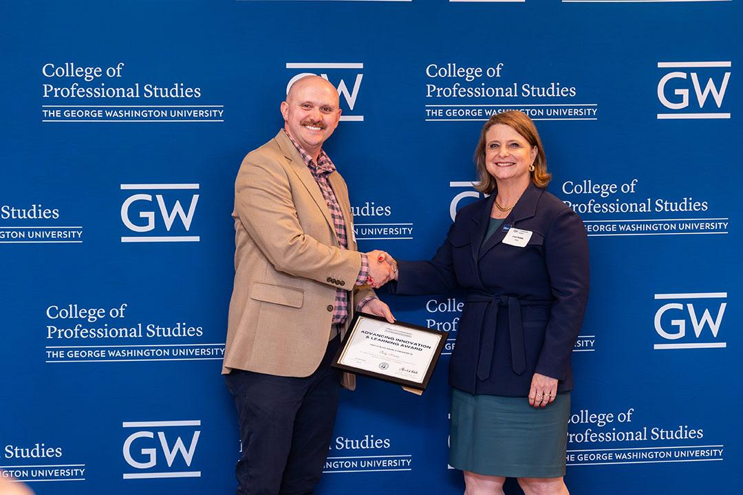 One man, one women with award frame in front of a GW blue background with logos.