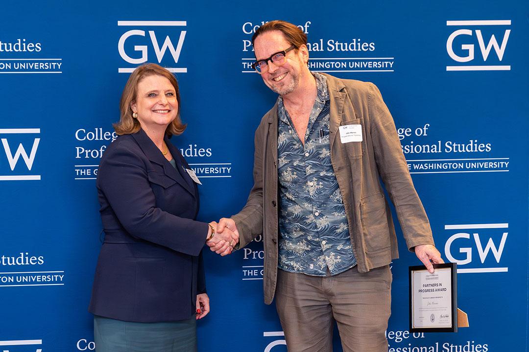 One man, one women with award frame in front of a GW blue background with logos.