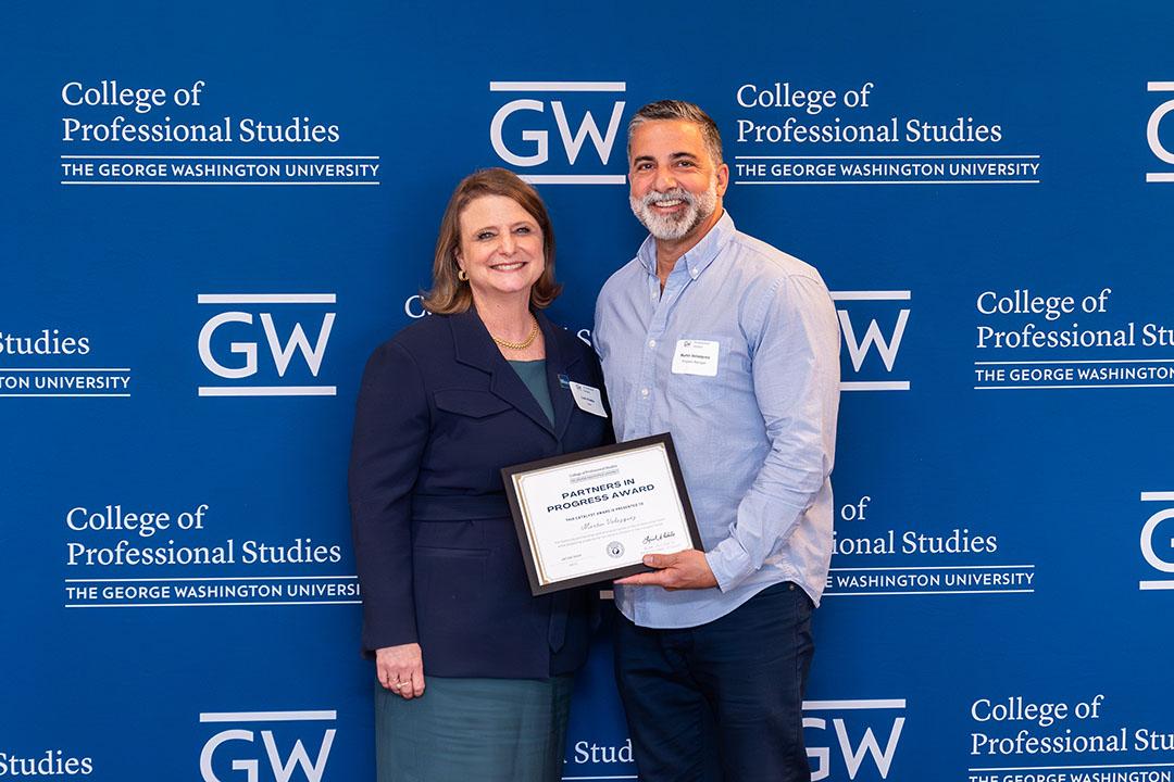 One man, one women with award frame in front of a GW blue background with logos.