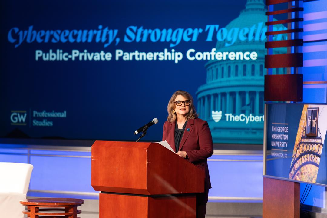 Liesl Riddle standing at a podium onstage in front of a screen that reads &quot;Cybersecurity, Stronger Together. Public-Private Partnership Conference